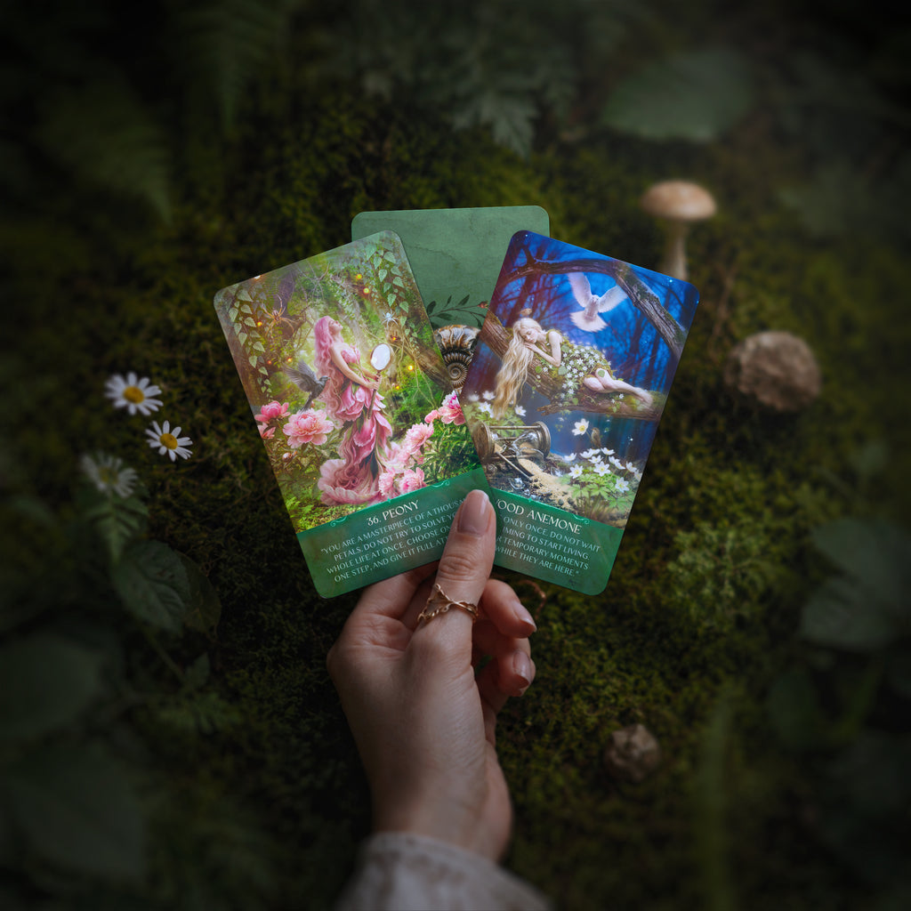 Hand holding three colorful Enchanted by Nature oracle cards on a mossy surface with flowers and mushrooms.
